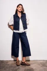 Chaleco de jean azul oscuro con cuello, bolsillos frontales y cierre con botones dorados. Corte al cuerpo.