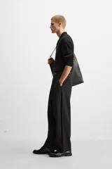 Pantalón negro de corte amplio, con pliegues en la parte delantera, bolsillos laterales y traseros de ojal.