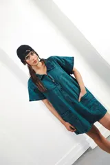 Vestido corto de denim celeste con cuello tipo camisa, cierre frontal metálico y bolsillos delanteros. Presenta bordados de soles y lunas en el canesú delantero y trasero.