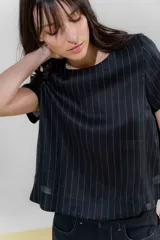 Blusa de lino color beige con rayas verticales negras, corte recto, escote redondo y mangas cortas.