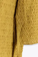 Top mostaza de cuello barco y manga larga con textura. Tiene lazadas ajustables en el bajo.