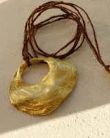 Collar con dije dorado en forma de concha marina y cordón marrón de seda natural.