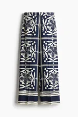 Pantalón de corte holgado con estampado de flores y hojas en azul y blanco. Modelo de tiro alto con elástico en la parte posterior de la cintura y cierre oculto con corchete en un lado. Bolsillos laterales discretos y piernas amplias con pliegues adelante y atrás.