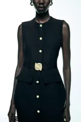 Vestido midi negro sin mangas, con cuello redondo, cinturón con hebilla metálica y cierre frontal con botones.