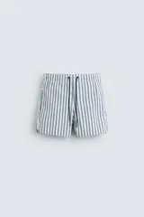 Bañador de hombre confeccionado en tejido técnico con textura. Diseño a rayas verticales en tonos azul y blanco. Cintura elástica ajustable con cordón. Bolsillos laterales y detalle de bolsillo trasero de solapa. Bajo con aberturas laterales. Forro interior.