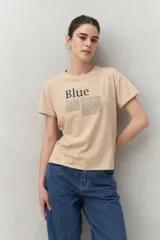 Remera color beige con estampado tipográfico azul al frente, de corte recto y manga corta.