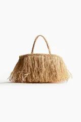 Bolso de mano tipo shopper confeccionado en paja de papel color natural con efecto desflecado. Tiene dos asas trenzadas y no está forrado.