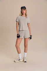 Remera deportiva color gris claro, de calce suelto, con mangas cortas, espalda abierta y logo de la marca en el ruedo.