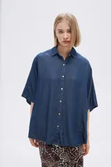 Camisa celeste de manga corta, corte holgado, con cuello camisero y cierre frontal con botones.