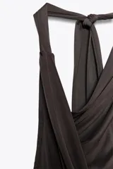 Vestido largo marrón oscuro con cuello halter y escote fluido. Tiene hombros descubiertos, detalle de pliegues laterales y forro interior a tono. Cierre lateral con cremallera oculta y en espalda con botones.