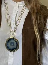 Collar con cadena de eslabones dorados y dije circular de bronce con piedra ágata en tonos celeste y azul.