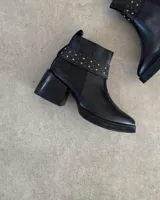 Botines negros de cuero con taco cuadrado y detalle de tachas doradas en el tobillo.