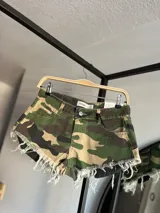 Short de jean con estampado de camuflaje en tonos verde, marrón y beige, con terminaciones desflecadas.