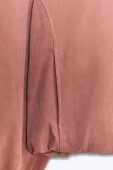 Chaqueta corta color rosa con capucha y manga larga terminada en puño. Tiene bolsillos de vivo en el delantero, bajo ajustable con cordones elásticos y cierre frontal con cremallera.