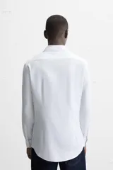 Camisa blanca de corte regular, cuello italiano, manga larga con puños abotonados y cierre frontal con botones.