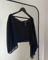 Poncho negro de tela traslúcida con mangas largas y corte irregular.