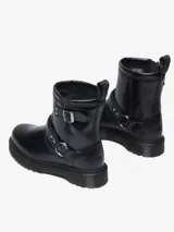Bota biker Dr. Martens Anistone Harness, color negro, confeccionada en cuero Orleans. Presenta correas con hebillas y herrajes en plata envejecida, incluyendo una argolla metálica en el lateral. Cuenta con tirador con logo en la parte trasera y suela Bex ligeramente elevada.