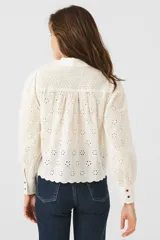 Blusa color crema con bordado inglés, cuello mao, mangas largas abullonadas y cierre frontal con botones.