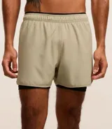 Bermuda deportiva color verde claro con short de compresión interno negro, cintura elástica con cordón ajustable y detalle reflectante trasero.
