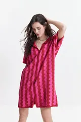 Vestido corto tejido de punto con cuello tipo camisa y cierre frontal con botones. Diseño a rayas verticales onduladas en tonos rosa y rojo.