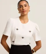 Blusa blanca de algodón con cuello redondo, mangas cortas abullonadas y bordados de abejas.