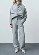 Pantalón gris de tiro medio y corte ancho, con bolsillos laterales, cierre oculto con botón, gancho y cremallera, y forro interior.