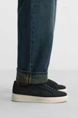 Zapatilla deportiva de hombre color gris topo, fabricada en piel con acabado serraje. Presenta cordonera elástica oculta y suela de goma de bajo volumen.