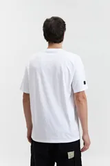 Remera blanca de manga corta con estampado frontal que incluye la palabra 'Savior' en letras cursivas negras y otros textos en tipografía sans-serif. Corte regular.