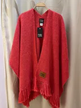 Ruana de punto color coral, con cuello en V y flecos en el dobladillo. Presenta una etiqueta de cuero sintético con el logo "Pura Lana" en la parte inferior derecha.