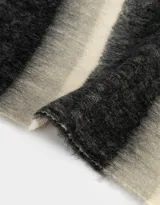 Bufanda tejida a rayas horizontales en tonos negro, gris y crema, con flecos en los extremos.
