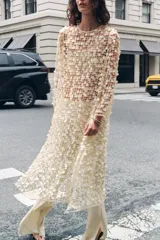 Vestido largo color crema con lentejuelas, de cuello redondo y manga larga. Tiene aberturas laterales en el bajo y cierre con abertura y botón en la espalda.