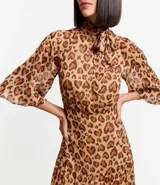 Vestido largo de chiffon con estampa de corazones con diseño de leopardo. Tiene cuello alto con lazo, mangas largas ligeramente transparentes y falda con volado. El tejido contiene hilo metalizado.