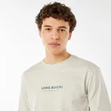 Remera color gris claro con estampado centrado en el pecho con la frase "Long Beach California" en color azul oscuro.