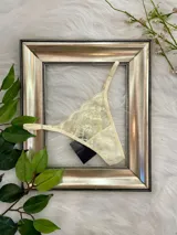 Tanga de encaje color champagne con ajuste regulable, confeccionado en tela suave y elástica con forro de algodón.
