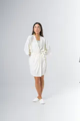 Bata tipo kimono de algodón color blanco hueso, con textura acanalada vertical. Presenta un cruce frontal asegurado con un lazo a la cintura y mangas anchas de largo al codo.