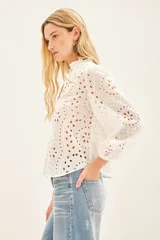 Camisa celeste de broderie de algodón con calado de hojas. Tiene cuello redondo con volados, mangas largas abullonadas con puños elásticos y cierre frontal con botones.