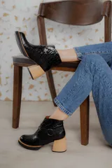 Botas cortas de cuero negro con textura tipo cocodrilo, caña alta, cierre con hebilla y taco de madera.