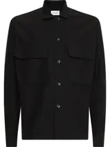 Sobrecamisa negra de sarga de algodón y nailon, corte boxy, cuello italiano, bolsillos con solapa en el pecho, billetera con botones, bajo recto, botones de gran tamaño e insignia con el logo de Calvin Klein en la manga.