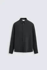 Camisa negra de corte relaxed fit confeccionada en tejido fluido con mezcla de viscosa. Tiene cuello solapa, manga larga con puño abotonado y cierre frontal con botones.