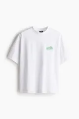 Remera blanca de algodón pesado con cuello redondo y estampado pequeño en el pecho. Corte oversized con hombros caídos y bajo recto.