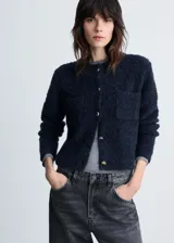 Chaqueta color celeste de tejido bouclé con cuello redondo, cierre frontal con botones efecto joya, dos bolsillos de parche frontales y mangas largas.