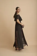 Vestido largo negro con transparencias y encaje. Tiene escote redondo, corte a la cintura y falda larga con paneles de encaje floral. El cuerpo superior es de gasa con hombros descubiertos y volado.