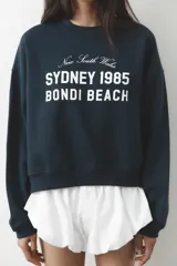 Sudadera azul marino de cuello redondo y manga larga con estampado frontal que dice "New South Wales Sydney 1985 Bondi Beach" en color blanco.