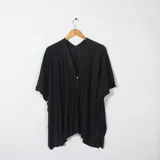 Ruana o poncho negro de tejido ligero, con escote en V y un solo botón frontal. Presenta un corte asimétrico y mangas cortas tipo murciélago.