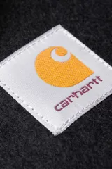 Bufanda de lana negra con flecos en los extremos y etiqueta cuadrada con el logo de Carhartt WIP en color blanco y naranja.