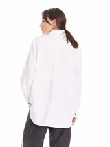 Camisa gris claro de tela Oxford, corte amplio, con cuello clásico, cierre frontal con botones negros, manga larga con puños abotonados, bolsillo de parche en el pecho y ruedo redondeado.