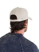 Gorro de béisbol color beige claro, confeccionado en sarga de algodón teñida con pigmentos. Presenta visera curva y el logo de Caterpillar (CAT) bordado en blanco en el panel frontal. Posee ajuste trasero con broche metálico.