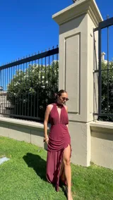 Vestido largo de microtul color rojo, con escote profundo en V y cuello halter. La falda presenta un diseño con frunces, transparencias y un tajo lateral pronunciado con detalle de volados.