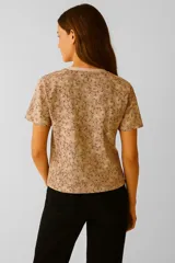 Remera de manga corta color marrón con estampado de flores en tonos beige y marrón oscuro, corte holgado y cuello redondo.