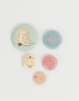 Set de cinco pines metálicos con diseños color pastel, incluyendo botas florales y mensajes inspiradores.